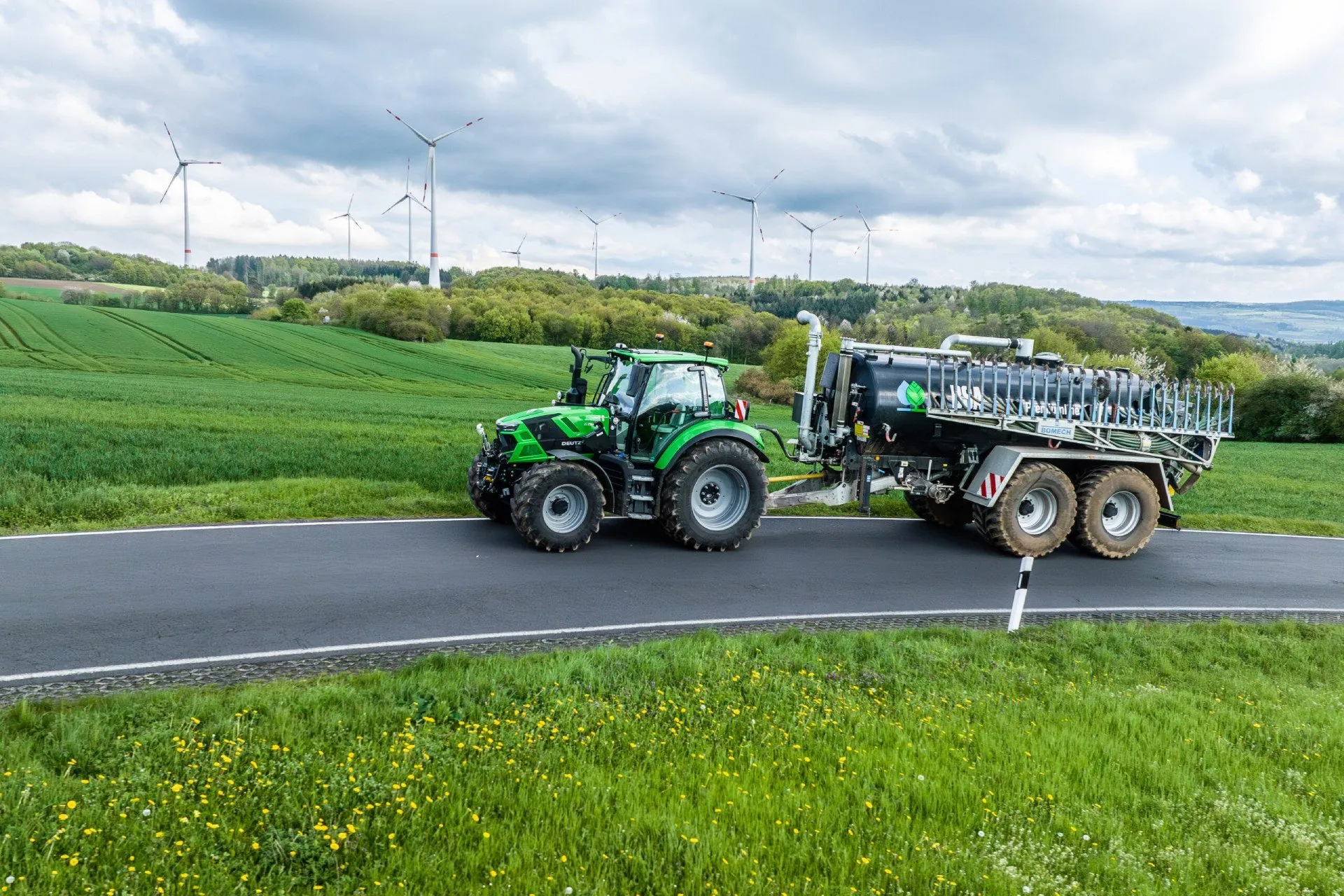 Grön Deutz-Fahr-traktor med tankvagn på en landsväg