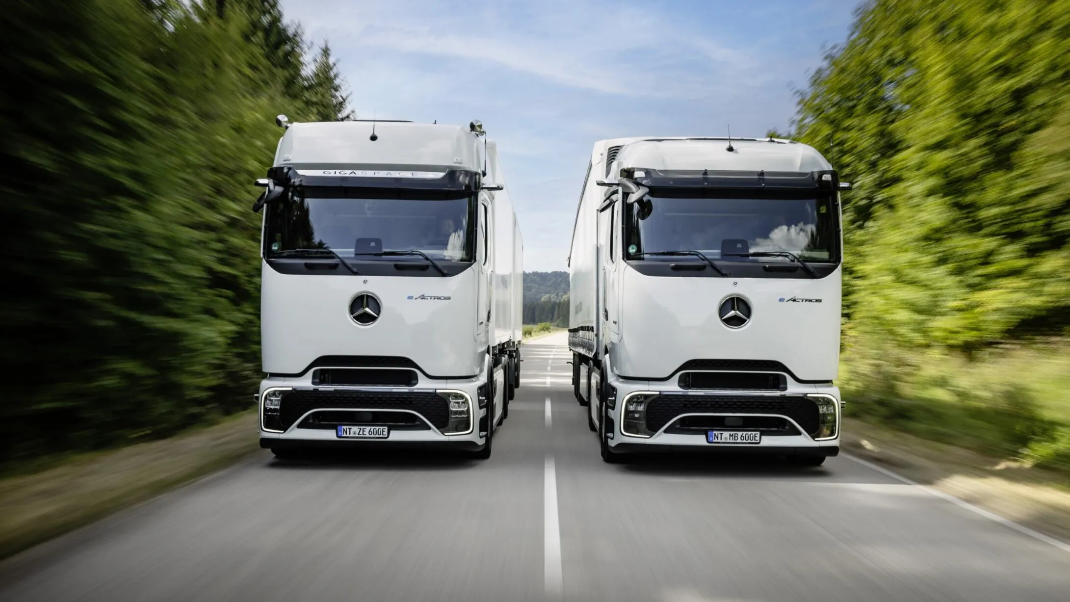 Två vita Mercedes-Benz-lastbilar på en väg